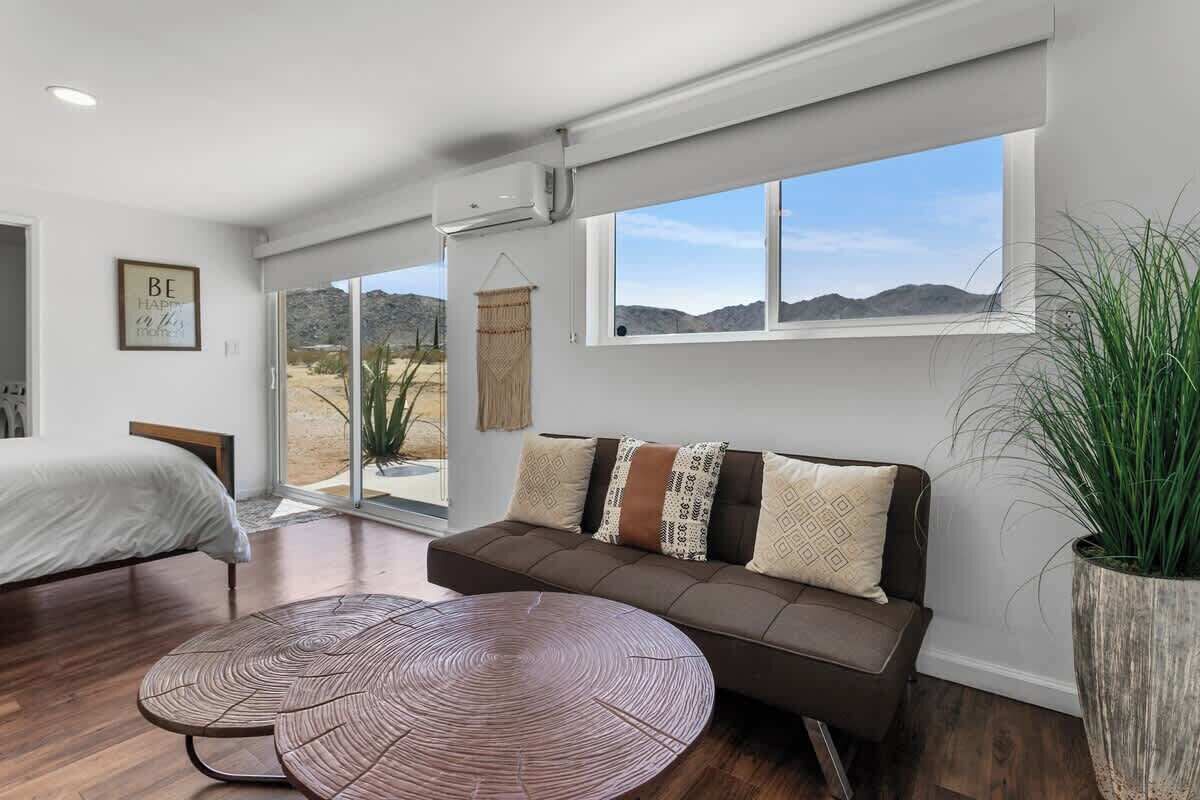 A modern living room with a sofa, a round coffee table, and a large window offering a view of the desert.