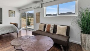 A modern living room with a sofa, a round coffee table, and a large window offering a view of the desert. - 4BR w/ Hot Tub, Space X & Tesla Charger! (Joshua Tree)
