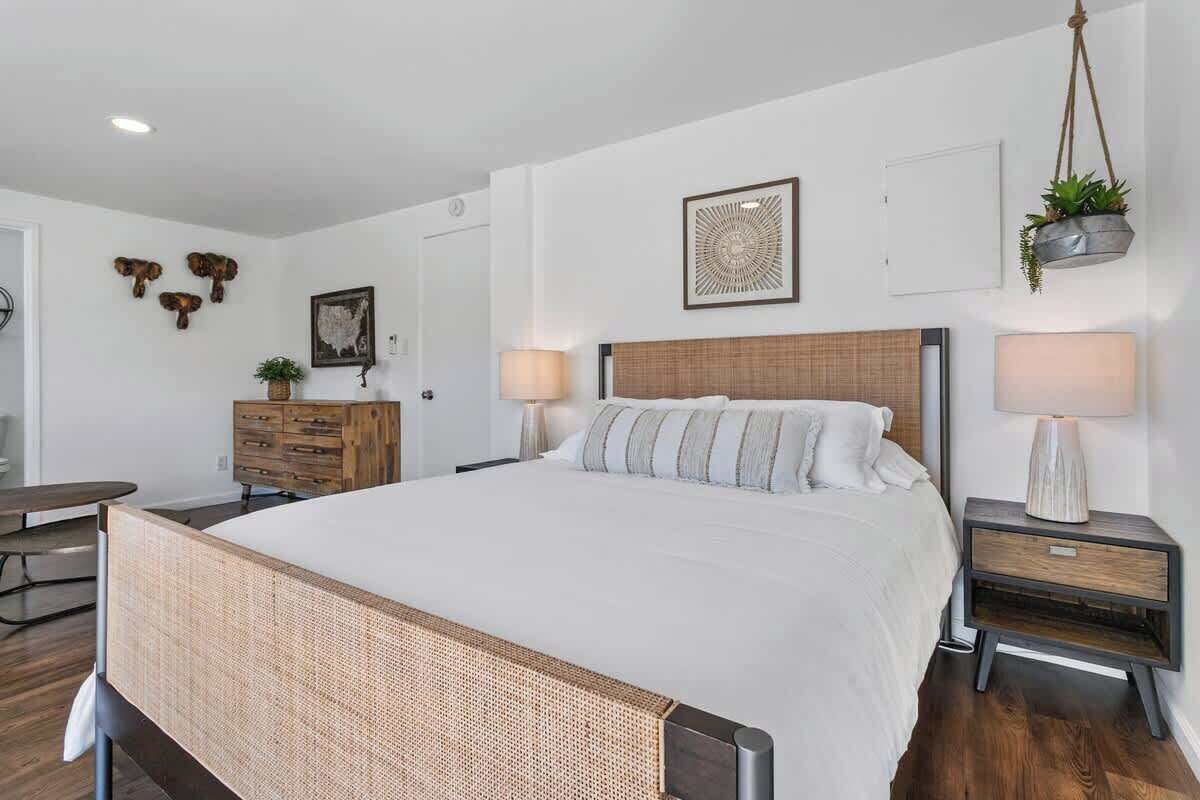 Un dormitorio moderno con una cama grande, mesitas de noche de madera, un aparador y decoración en la pared.