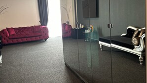 A modern room with a red sofa, a black sofa, a glass partition, and a flat-screen TV on the wall. - Firstclass Event & Hotel (Fuerth)