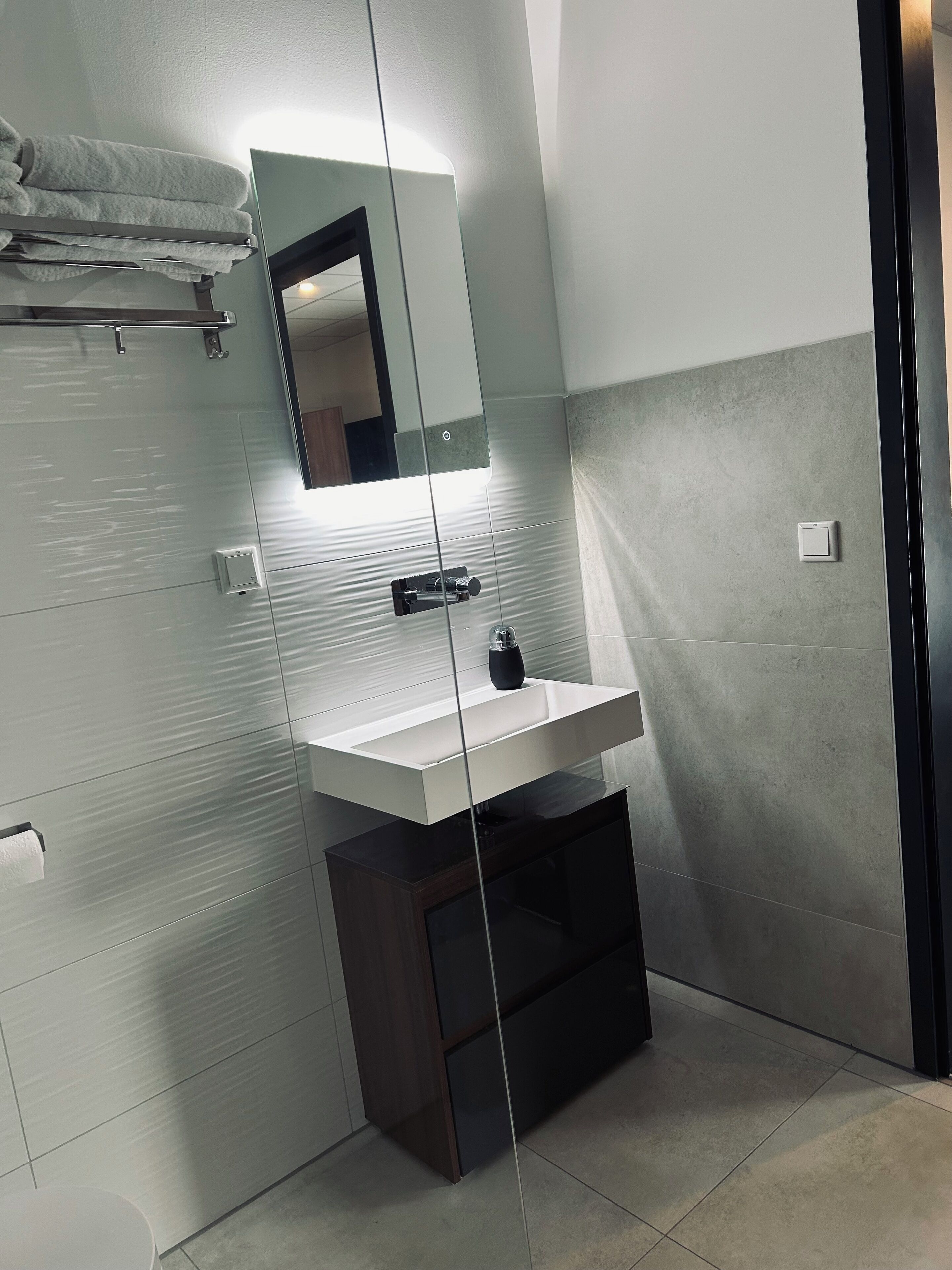 Un baño moderno con mampara de vidrio, lavamanos blanco y barra para toallas.