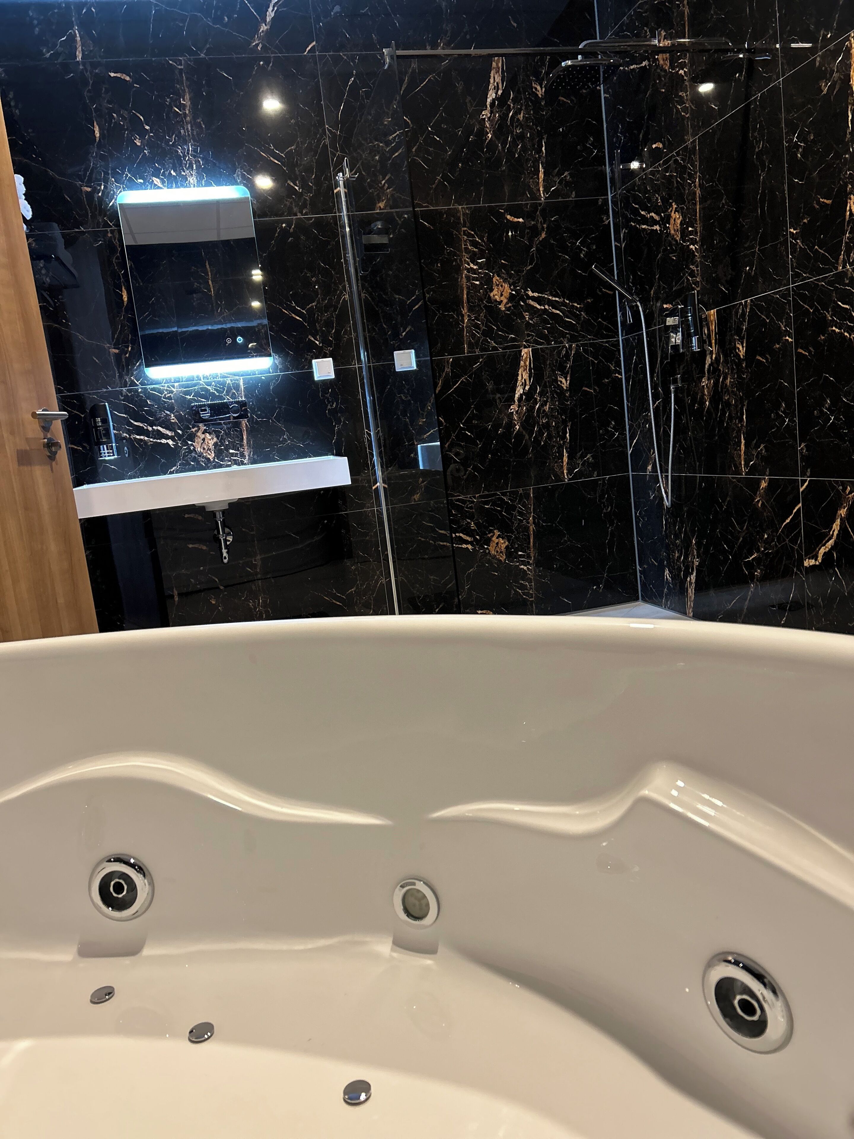 Un baño moderno con salpicadero de mármol, una bañera blanca y un estante empotrado con artículos de aseo.