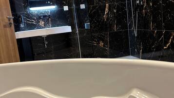 Un baño moderno con salpicadero de mármol, una bañera blanca y un estante empotrado con artículos de aseo.