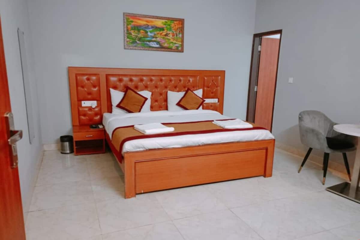 Una cama bien tendida con cabecera de madera, una mesita de noche, un cesto de basura y una silla.