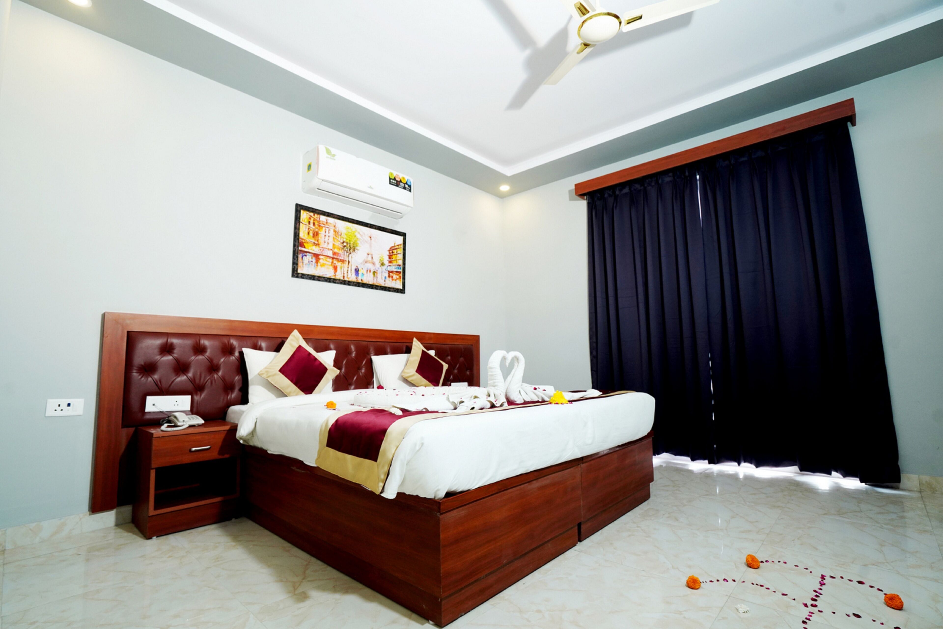 A hotel room with a wooden bed, a nightstand, a wall-mounted air conditioner, a framed picture, and a large window with dark curtains.