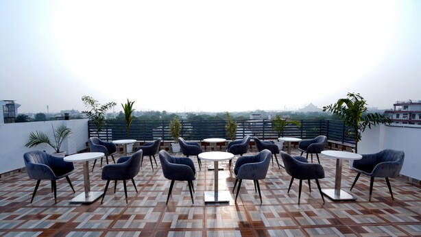 A rooftop terrace with multiple round tables and chairs, a patterned floor, and a view of distant buildings. - ExpoMart Inn (Greater Noida)