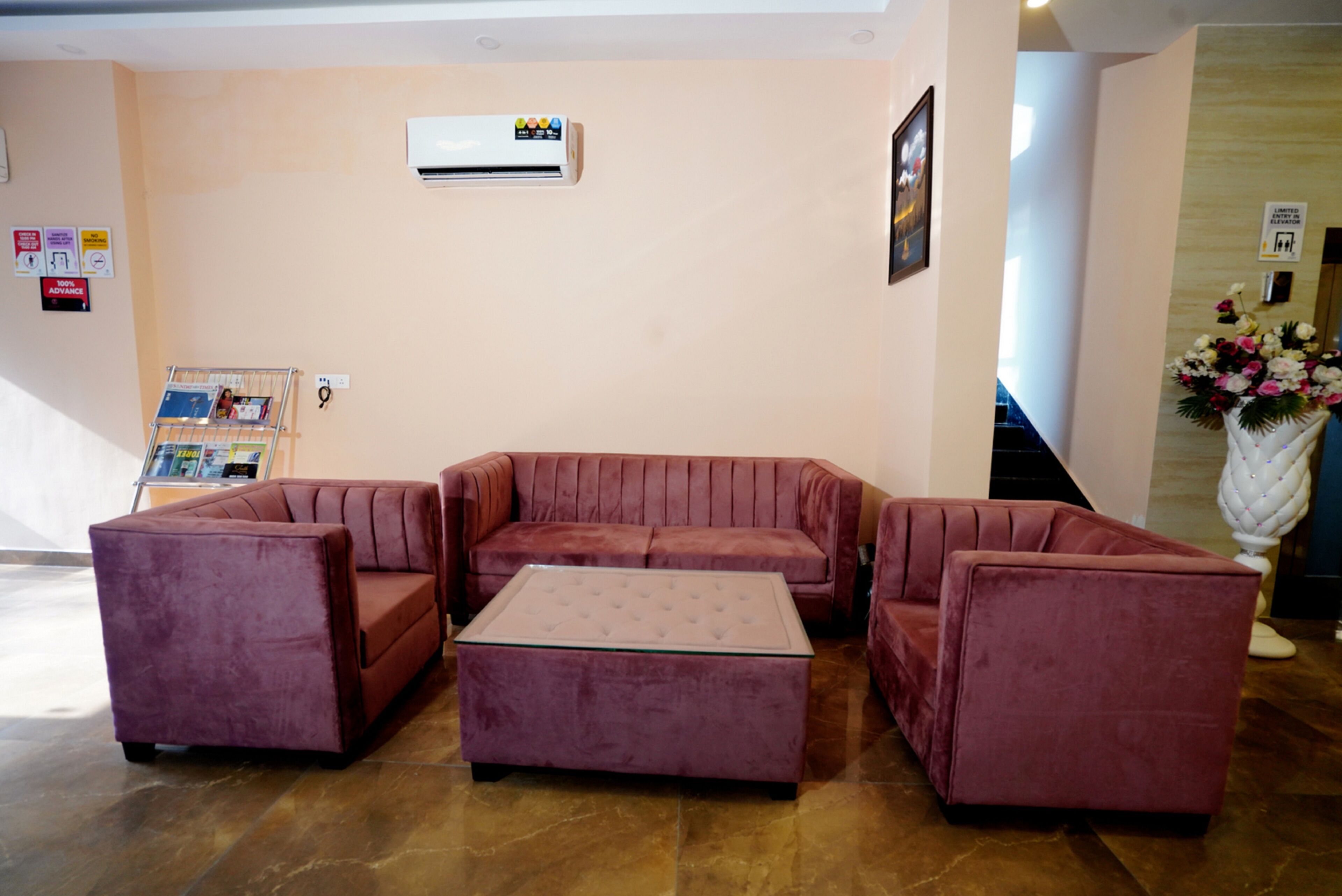 A lobby with a red sofa set, a glass-top coffee table, and a wall-mounted air conditioner.