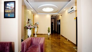 A hotel lobby with a marble floor, a reception desk, a red chair, and a framed picture on the wall. - ExpoMart Inn (Greater Noida)