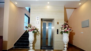 An elevator in a lobby with two white vases of flowers on either side. - ExpoMart Inn (Greater Noida)
