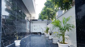 A clean, modern indoor space with a polished marble floor, several potted plants, and a visible electrical panel. - ExpoMart Inn (Greater Noida)