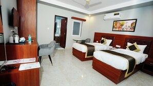 A hotel room with two beds, a desk with a chair, a television, and a ceiling fan. - ExpoMart Inn (Greater Noida)