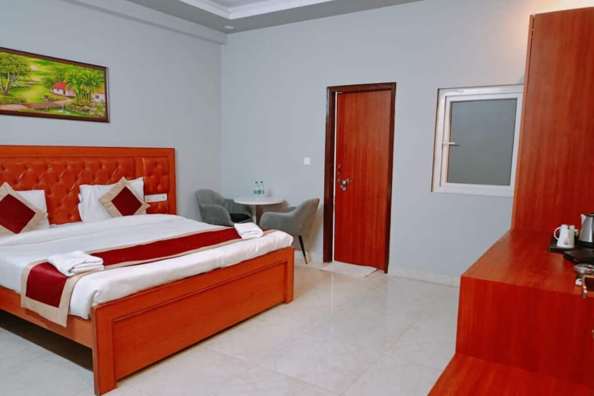 Una habitación de hotel con una cama grande, una mesita pequeña, una silla, un armario de madera y un cuadro en la pared.