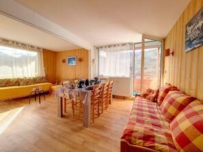 Tunnelmallinen huone, jossa on ruokapöytä, tuoleja, sohva ja suuri ikkuna, josta avautuu näkymä ulos.