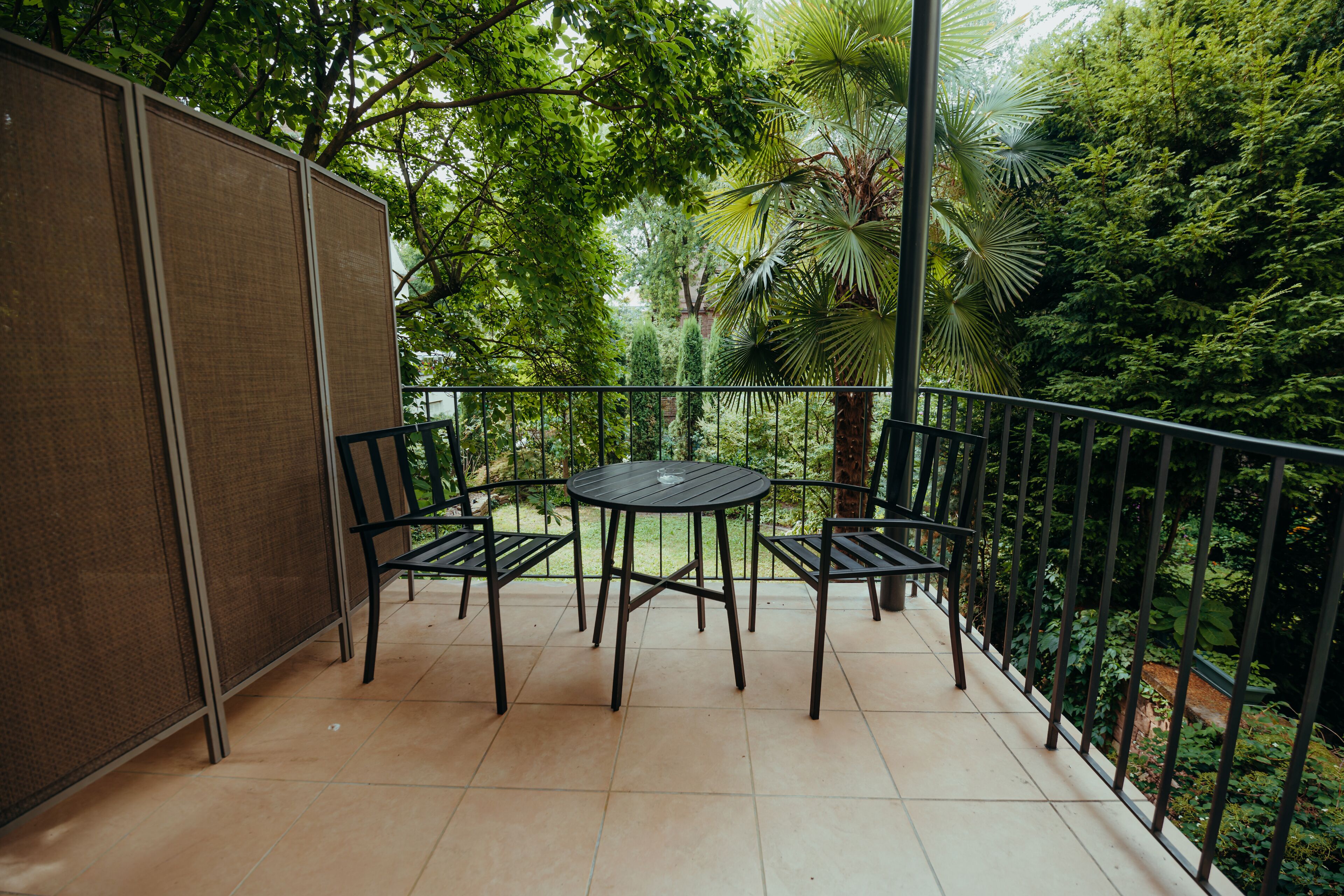 A balcony with a table and chairs, surrounded by lush greenery.