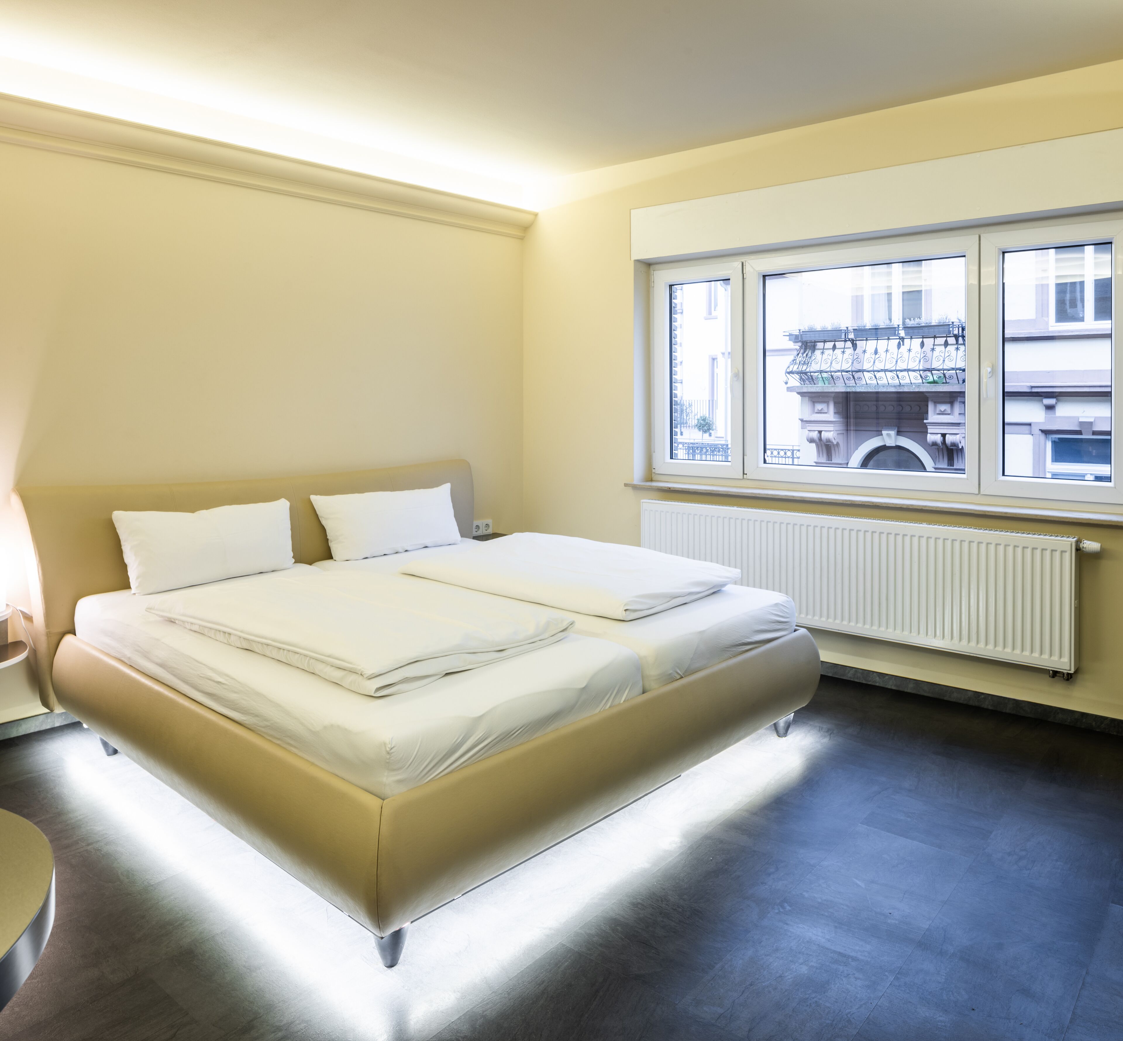 Un letto matrimoniale in una stanza con finestra, termosifone e una sedia.