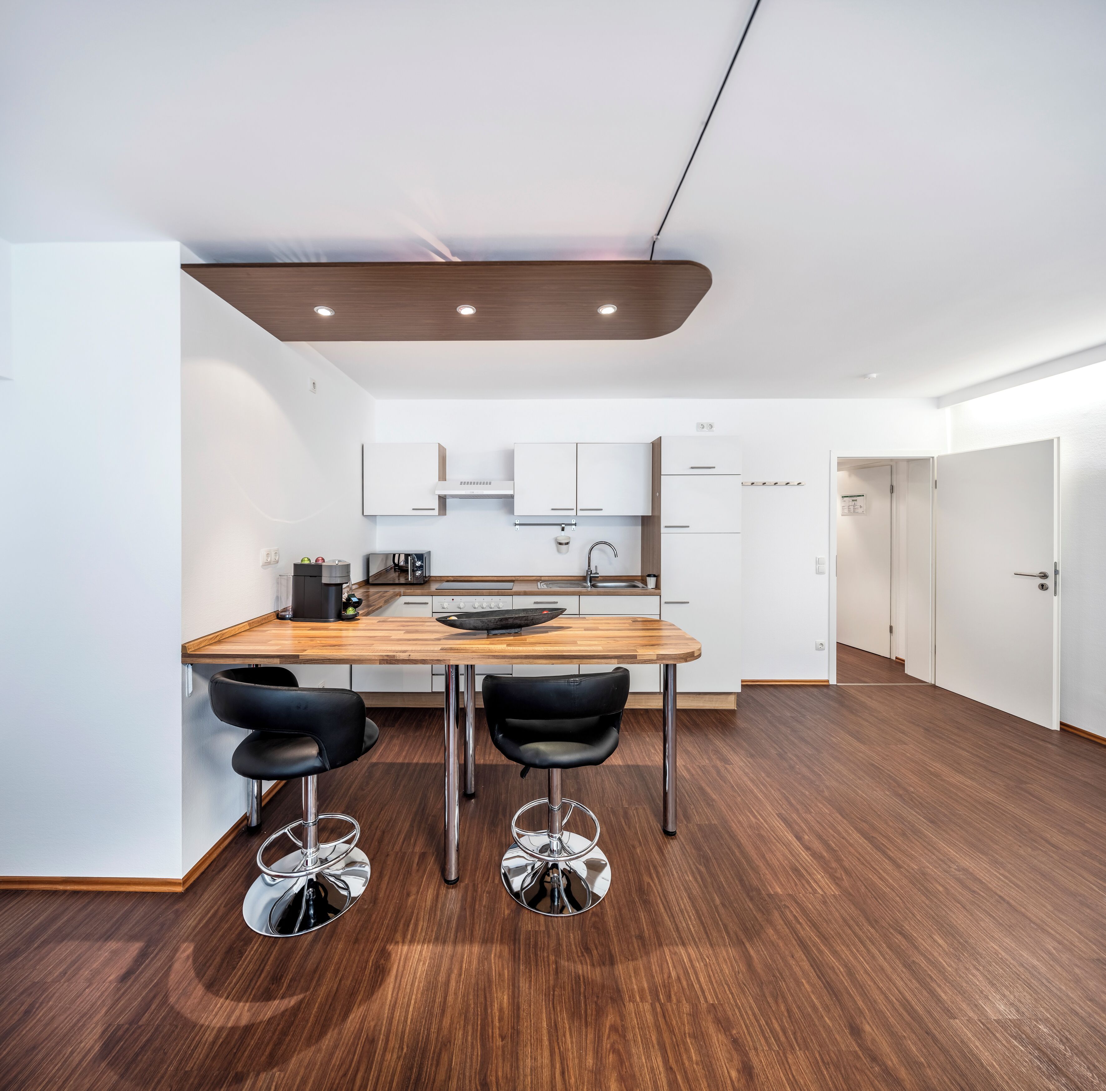 A modern kitchen with a wooden island, two black bar stools, white cabinets, and a stainless steel sink.