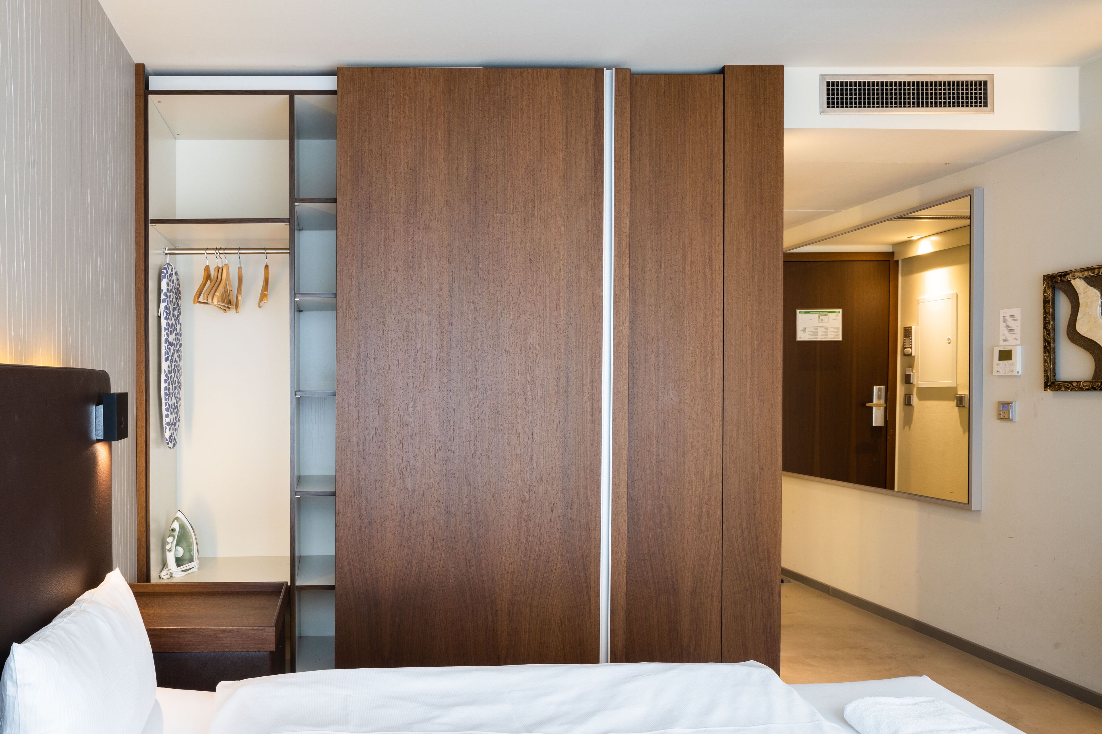 Habitación de hotel con cama, armario, espejo y zona de ducha.