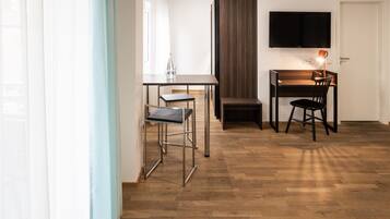 Una habitación moderna con piso de madera, una mesa de comedor con dos sillas, un televisor montado en la pared y un ventanal con cortinas.