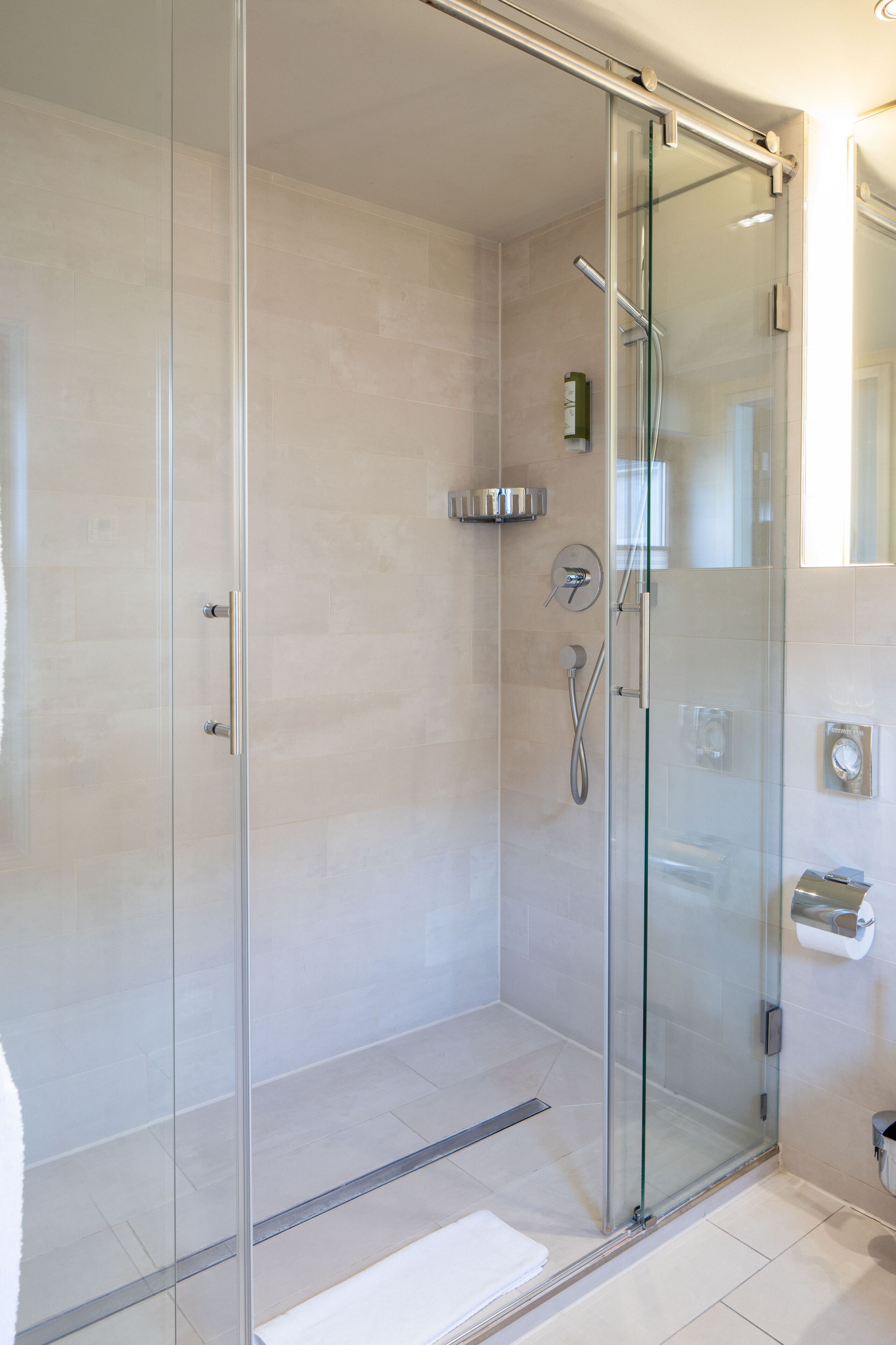 A glass-enclosed shower with a handheld showerhead and a wall-mounted faucet.