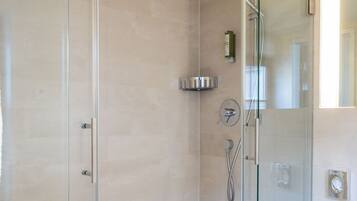 A glass-enclosed shower with a handheld showerhead and a wall-mounted faucet.