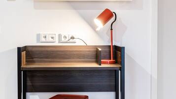Ein moderner Arbeitsplatz mit einem Holztisch, einem roten Hocker, einem montierten Fernseher und einer roten Schreibtischlampe.
