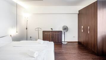 Ein modernes Hotelzimmer mit einem großen Bett, einem Holzschrank, einem Schreibtisch und einem Standventilator.
