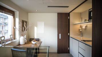 Una cocina moderna con zona de comedor, que incluye una mesa de madera, sillas, un florero con ramas y vistas a la ciudad a través de una ventana.