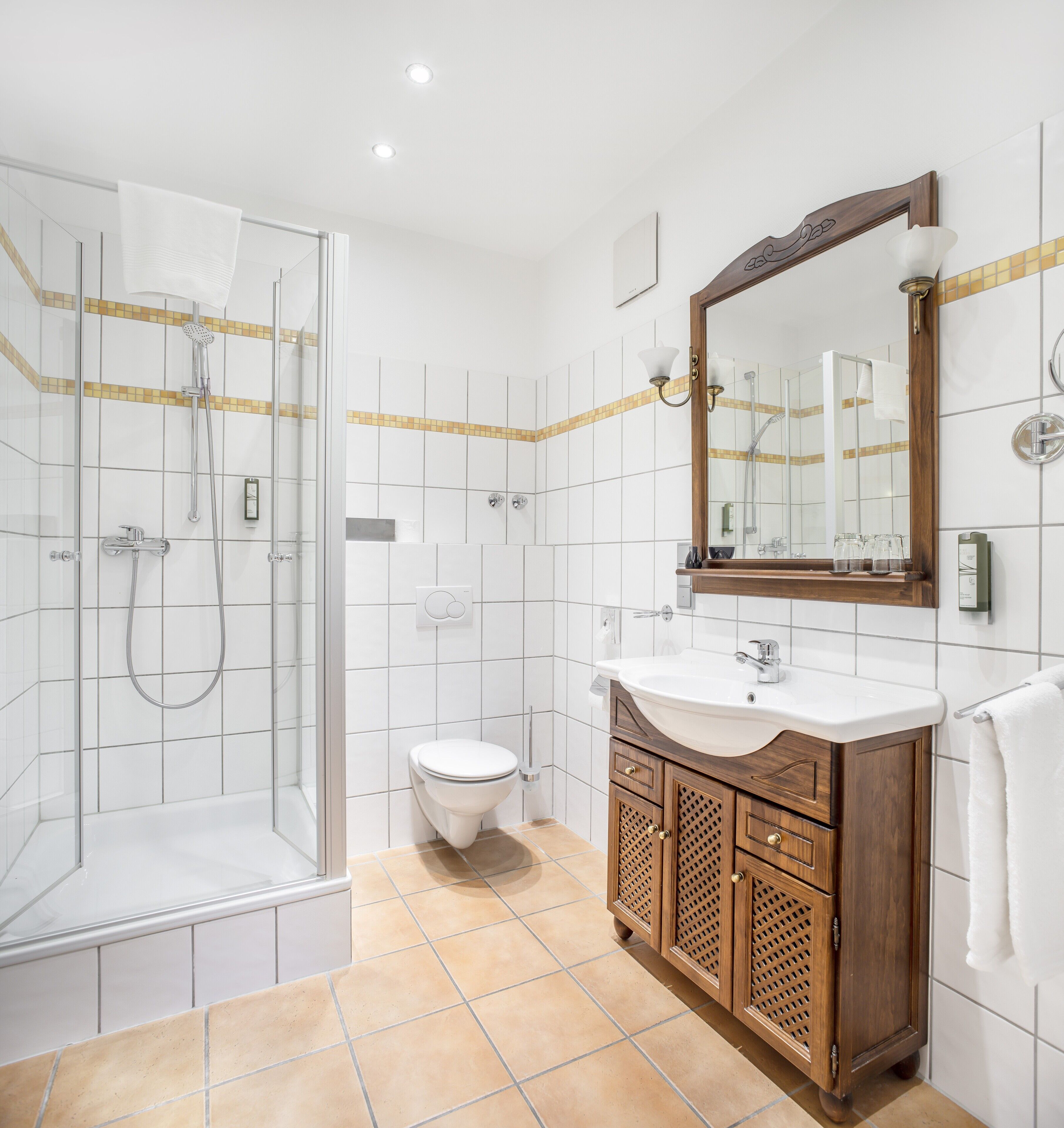A modern bathroom with a glass-enclosed shower, a white toilet, a wooden vanity with a mirror, and a tiled floor.