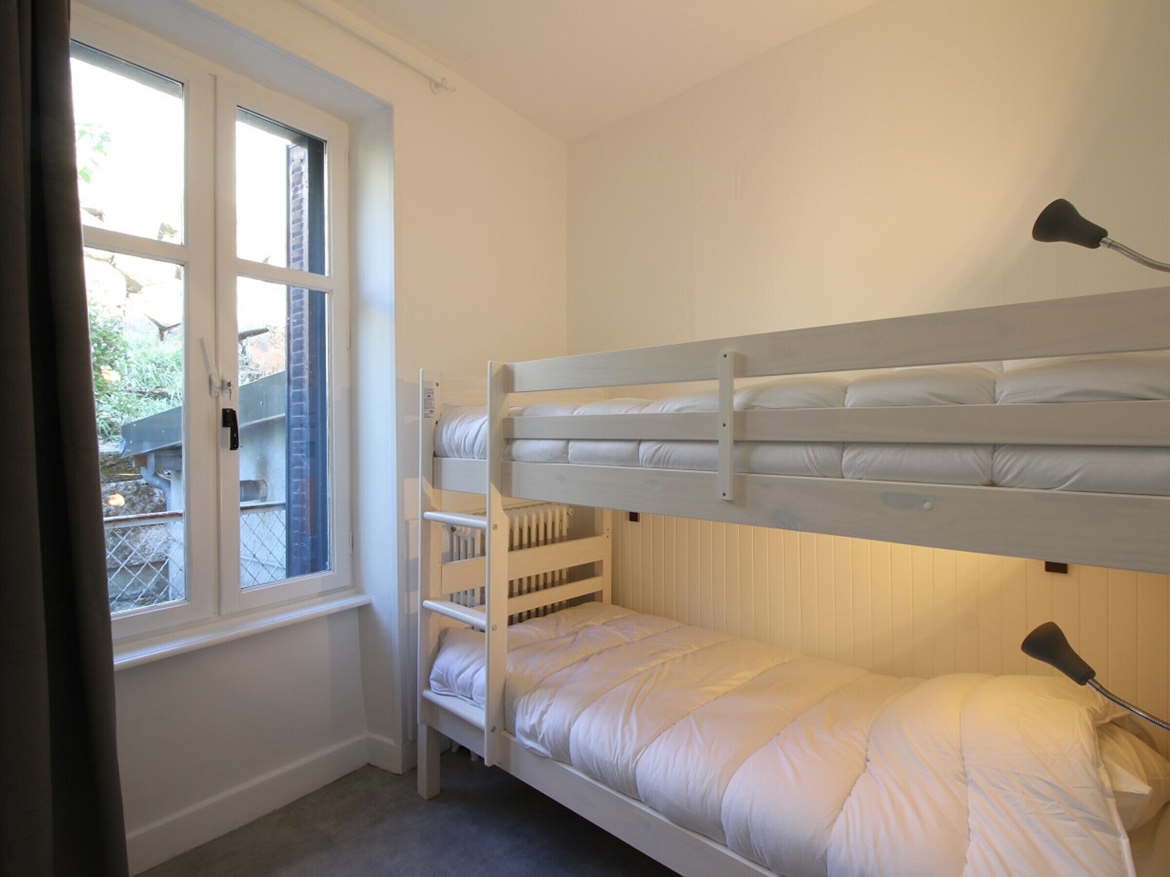 A bunk bed room with a window, a radiator, and a lamp.