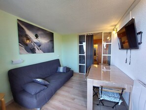 Cozy living space with a sofa, flat-screen TV, and large window offering a view.