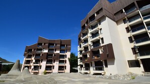A modern multi-story building with balconies, a parking area, and a clear blue sky. - Ski-in/Ski-out Apartment in Reberty 1850, Les Menuires - Sleeps 4, 1 Bed, 1 Bath (Les Menuires)