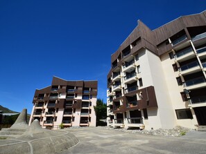 Moderni, useita kerroksia sisältävä rakennus, jossa on parvekkeet, pysäköintialue ja kirkkaan sininen taivas.
