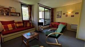A cozy living room with a sofa, a rocking chair, a small table, and a dining area with a table and chairs. - Ski-in/Ski-out Apartment in Reberty 1850, Les Menuires - Sleeps 4, 1 Bed, 1 Bath (Les Menuires)