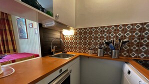A compact kitchen with a sink, stove, and dishwasher. There is a decorative backsplash and a small shelf with kitchen utensils. - Ski-in/Ski-out Apartment in Reberty 1850, Les Menuires - Sleeps 4, 1 Bed, 1 Bath (Les Menuires)