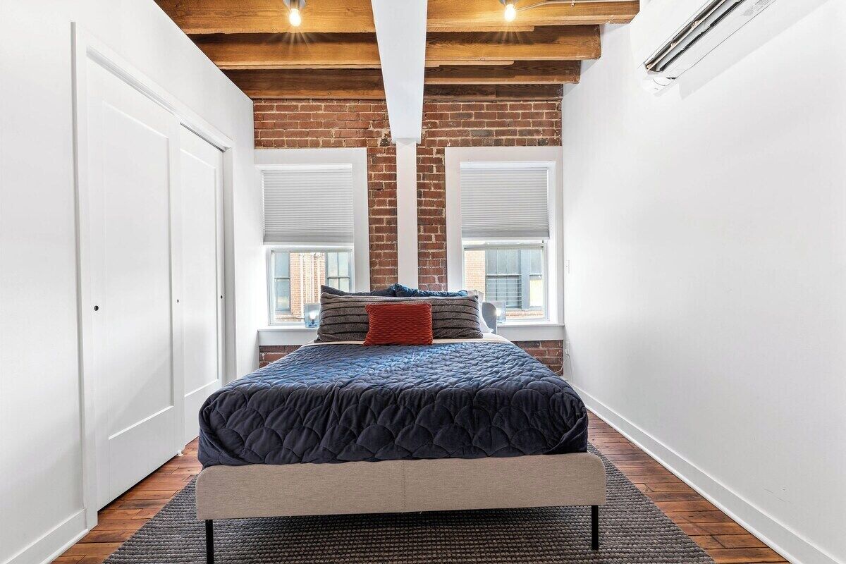 A bedroom with a bed, a bench, a window, and a brick wall.