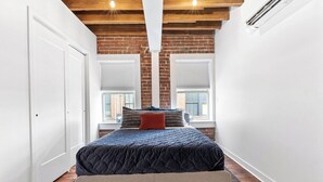 Ein Schlafzimmer mit einem Bett, einer Bank, einem Fenster und einer Backsteinwand.