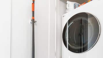 A laundry room with a washing machine, a dryer, and a broom leaning against the wall.