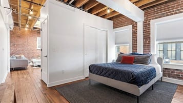 A bedroom with a bed, a wardrobe, a window with blinds, and a brick wall.