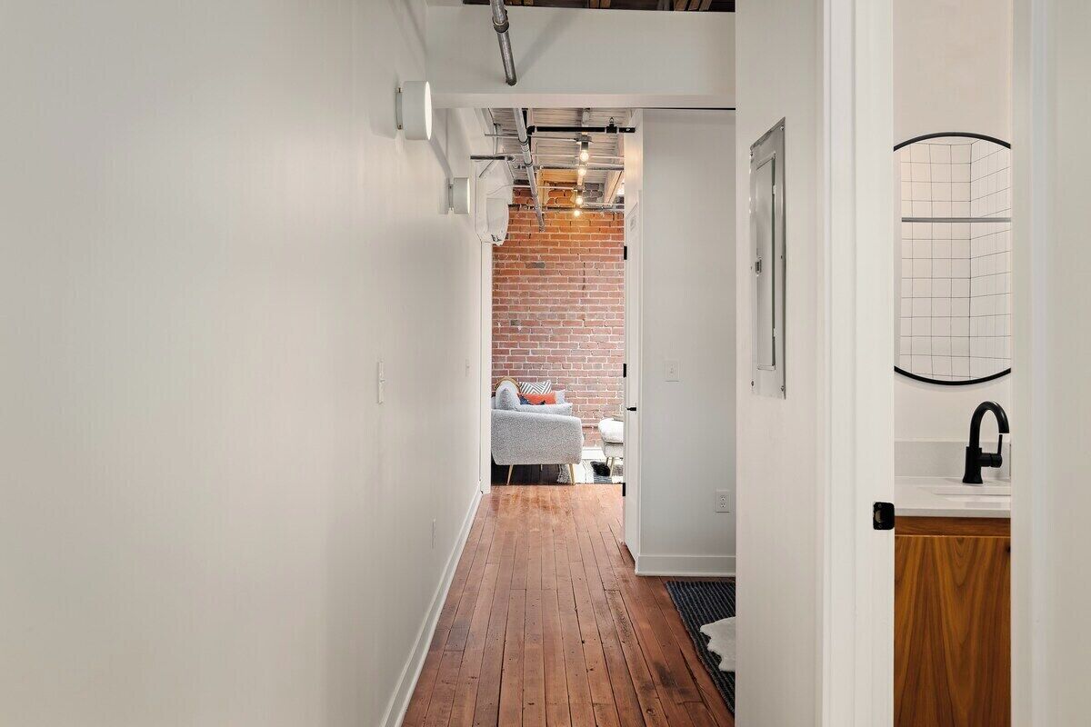 A narrow hallway with wooden flooring, white walls, and a brick wall in the background.