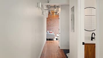 A narrow hallway with wooden flooring, white walls, and a brick wall in the background.