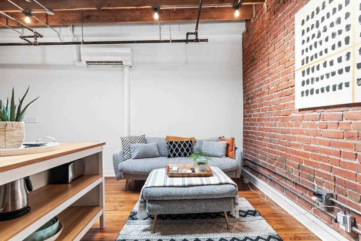 A cozy living area with a sofa, ottoman, and a dining table with a plant.