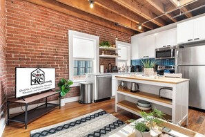 A modern kitchen with a brick wall, stainless steel appliances, and a wooden dining table.