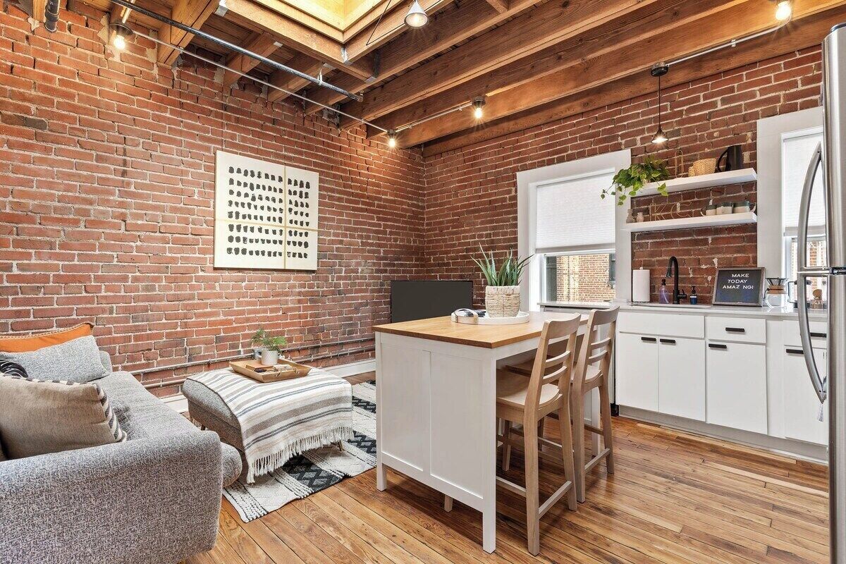 A cozy kitchen with a brick wall, wooden ceiling, and a white countertop.