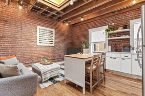 A cozy kitchen with a brick wall, wooden ceiling, and a white countertop.