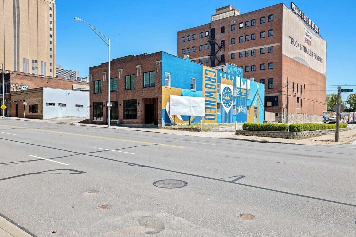 A street with a building featuring a large mural, a clear sky, and a road with marked lanes.