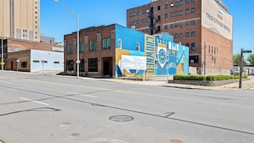 A street with a building featuring a large mural, a clear sky, and a road with marked lanes.