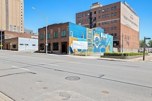 Una calle con un edificio que presenta un gran mural, cielo despejado y una carretera con carriles señalizados.