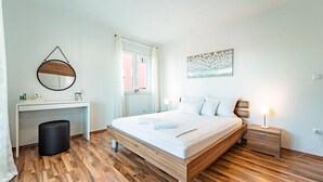 A bedroom with a wooden bed, a bedside table with a lamp, a round mirror, a desk with toiletries, and a window with curtains. - Amazing apartment in Biograd na Moru with WiFi (Biograd na Moru)