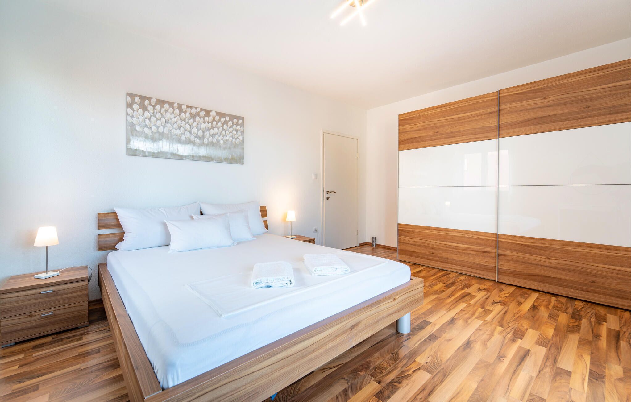 Une chambre à coucher moderne avec un lit en bois, du linge de lit blanc, une lampe de chevet et une grande armoire.