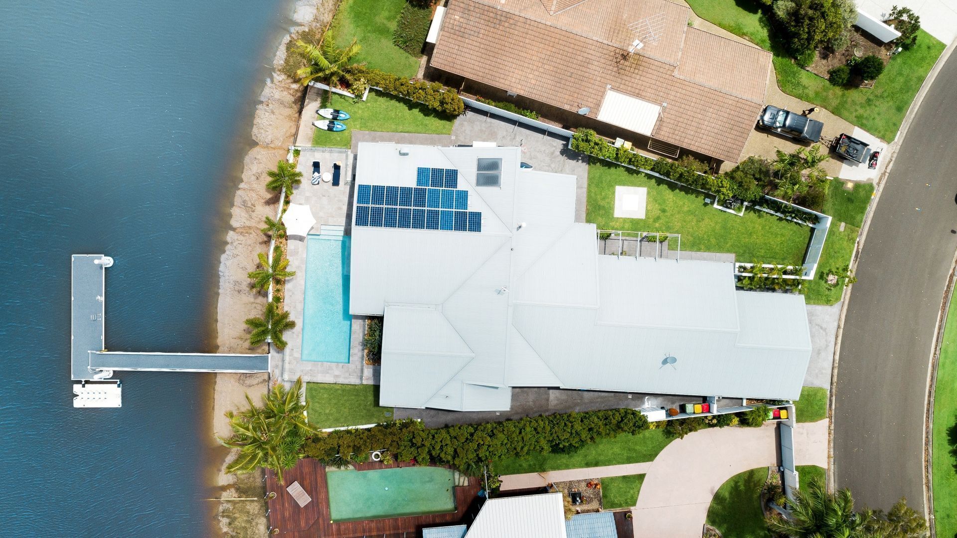 A house with a swimming pool, solar panels, and a dock by the water.